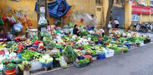 ハノイ旧市街のドンスアン市場の場外で野菜を売る商人たちと並べられた大量の商品の写真