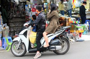 ドンスアン市場の横の雑貨と金物を売る店で、バイクに乗ったまま買い物する若いベトナム人カップルの写真。