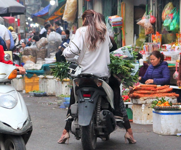 ハノイ旧市街ドンスアン市場の場外売り場で大量の野菜を買うバイクの若い女性の写真